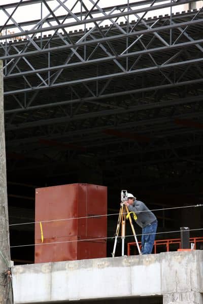 Surveyor using total station equipment to perform an ALTA Land Title Survey on a retail construction site
