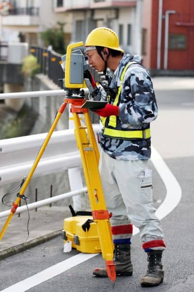 Land surveyor using total station equipment to measure property boundaries during rezoning work
