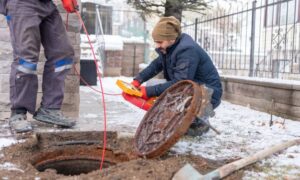 Utility line inspection alta survey - ALTA SURVEY Dallas Technicians inspecting an underground utility access point near a home, representing how an ALTA survey helps document service lines and hidden utilities.